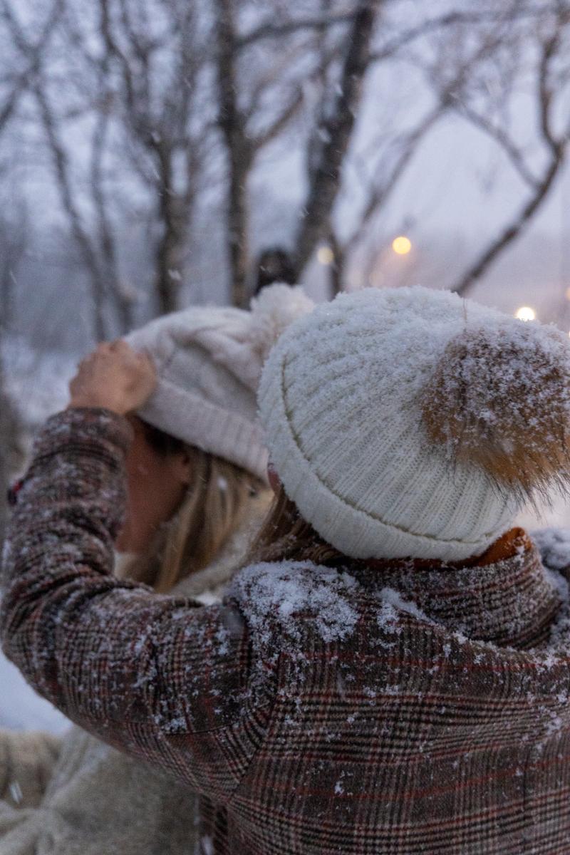 Rette på lua i snø.jfif To personer ute i snøen. Den ene retter på lua til den andre.